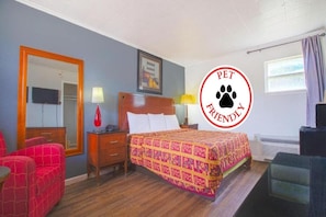 A pet-friendly hotel room with a bed, a desk, a chair, a mirror, and a window.