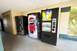 Eine Reihe von Verkaufsautomaten, darunter ein Automat mit Pepsi-Branding, in einem Korridor mit beigen Wänden und einem Betonboden.