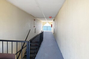 A narrow hallway with a metal railing on one side, a blue door at the end, and a red exit sign on the ceiling. - King Bed with Kitchenette Non-Smoking (Milledgeville, GA)