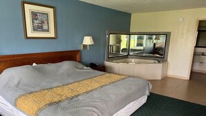 A hotel room with a bed, a bathroom with a mirror, a sink, and a framed picture on the wall. - King Bed with Kitchenette Non-Smoking (Milledgeville, GA)