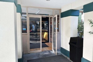 A building entrance with a glass door, a trash bin, and a small indoor area with a counter. - King Bed with Kitchenette Non-Smoking (Milledgeville, GA)