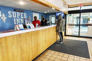 A hotel reception desk with a blue wall, a digital clock, and a sign reading 'Super Inn.'