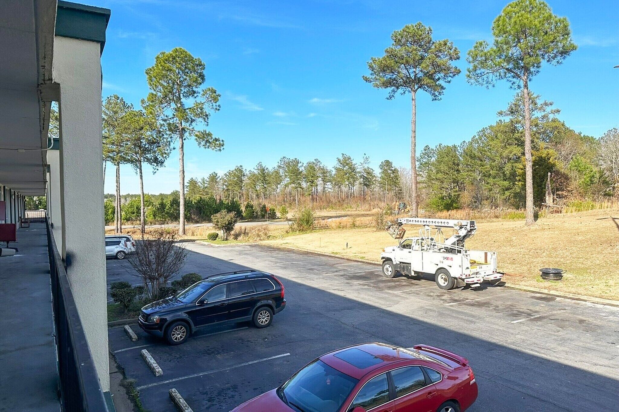 A parking lot with a few cars, a utility truck, and a building with a balcony.