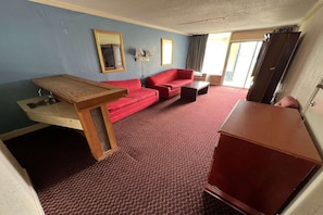 Hotellihuone, jossa on puinen työpöytä, kaksi punaista sohvaa, pieni pöytä, peili ja vaatekaappi.
