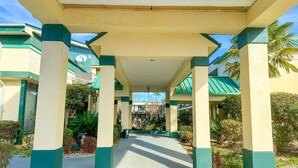 A covered walkway with columns, leading to a building with a green roof.