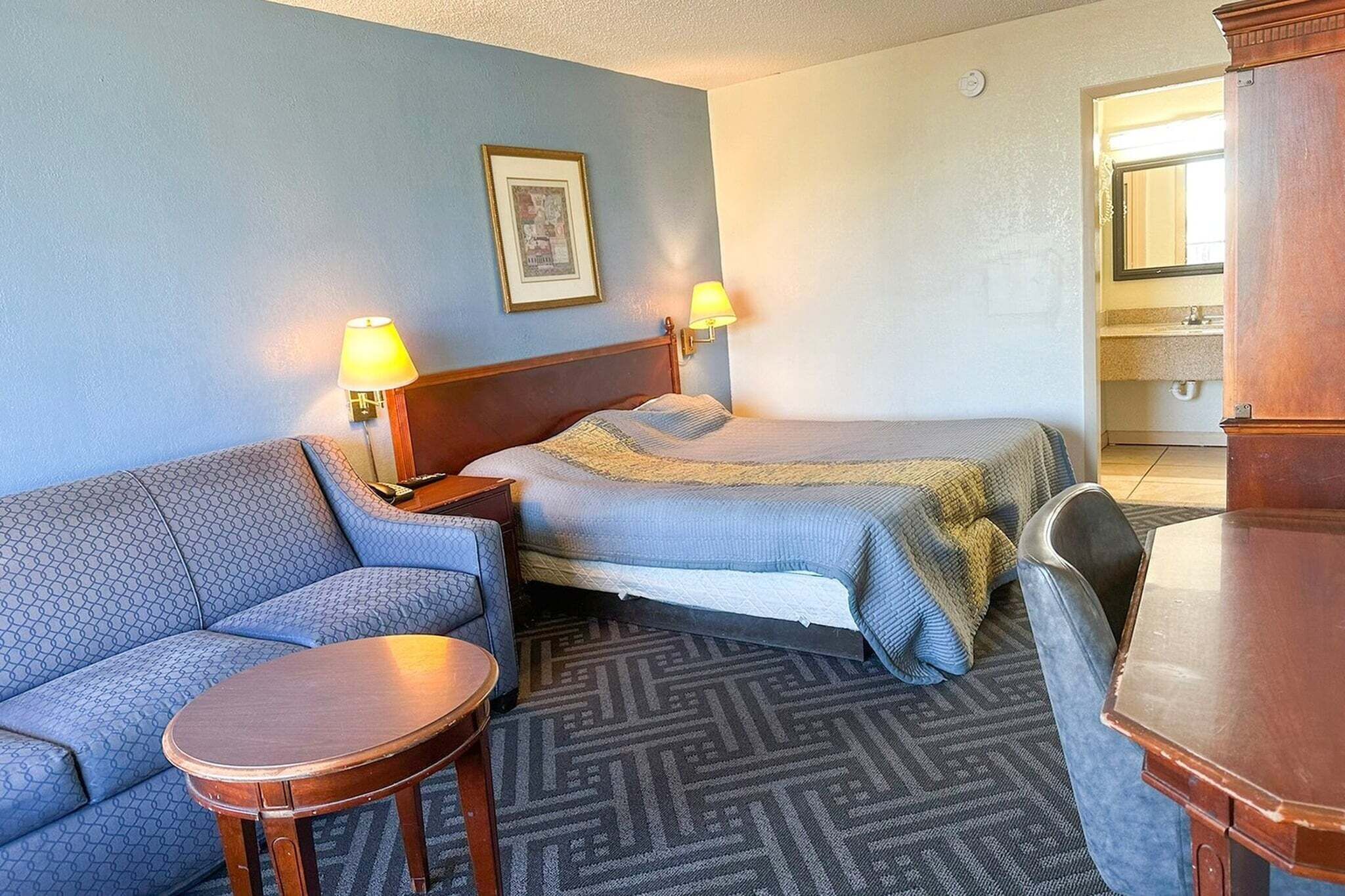 A hotel room with a sofa, two single beds, a small table, a lamp, and a mirror.