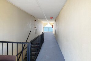 Un passadís estret amb una escala a l'esquerra, una porta blava al final i un senyal vermell d'emergència al sostre.
