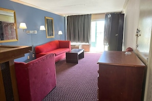 Una habitación de hotel con un sofá rojo, un escritorio de madera, una mesita pequeña y un espejo.