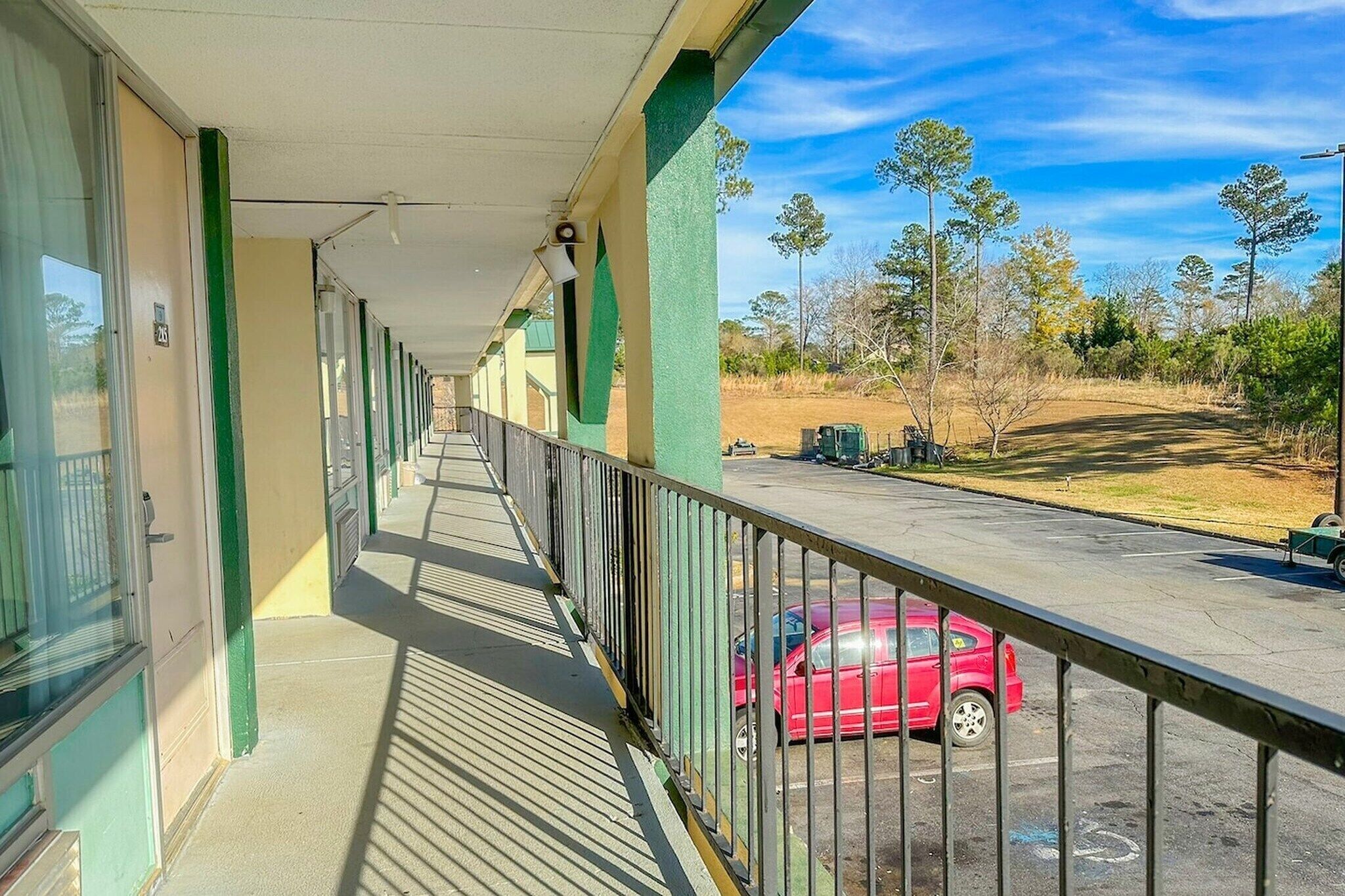 A covered walkway with a view of a parking area and trees.