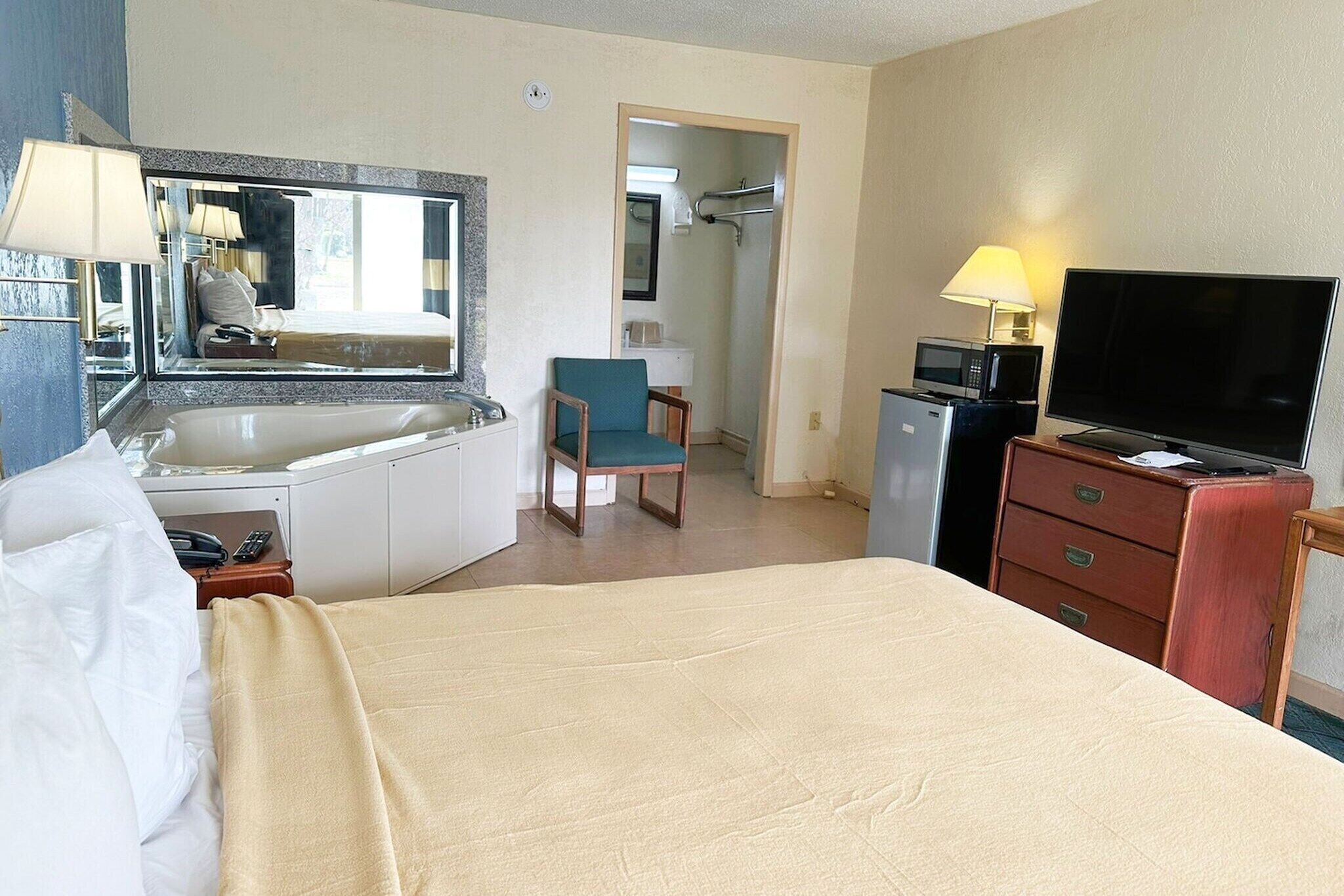 Een hotelkamer met een bed, een bureau met spiegel, een stoel, een televisie, een magnetron en een kleine kitchenette.
