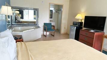 Een hotelkamer met een bed, een bureau met spiegel, een stoel, een televisie, een magnetron en een kleine kitchenette.
