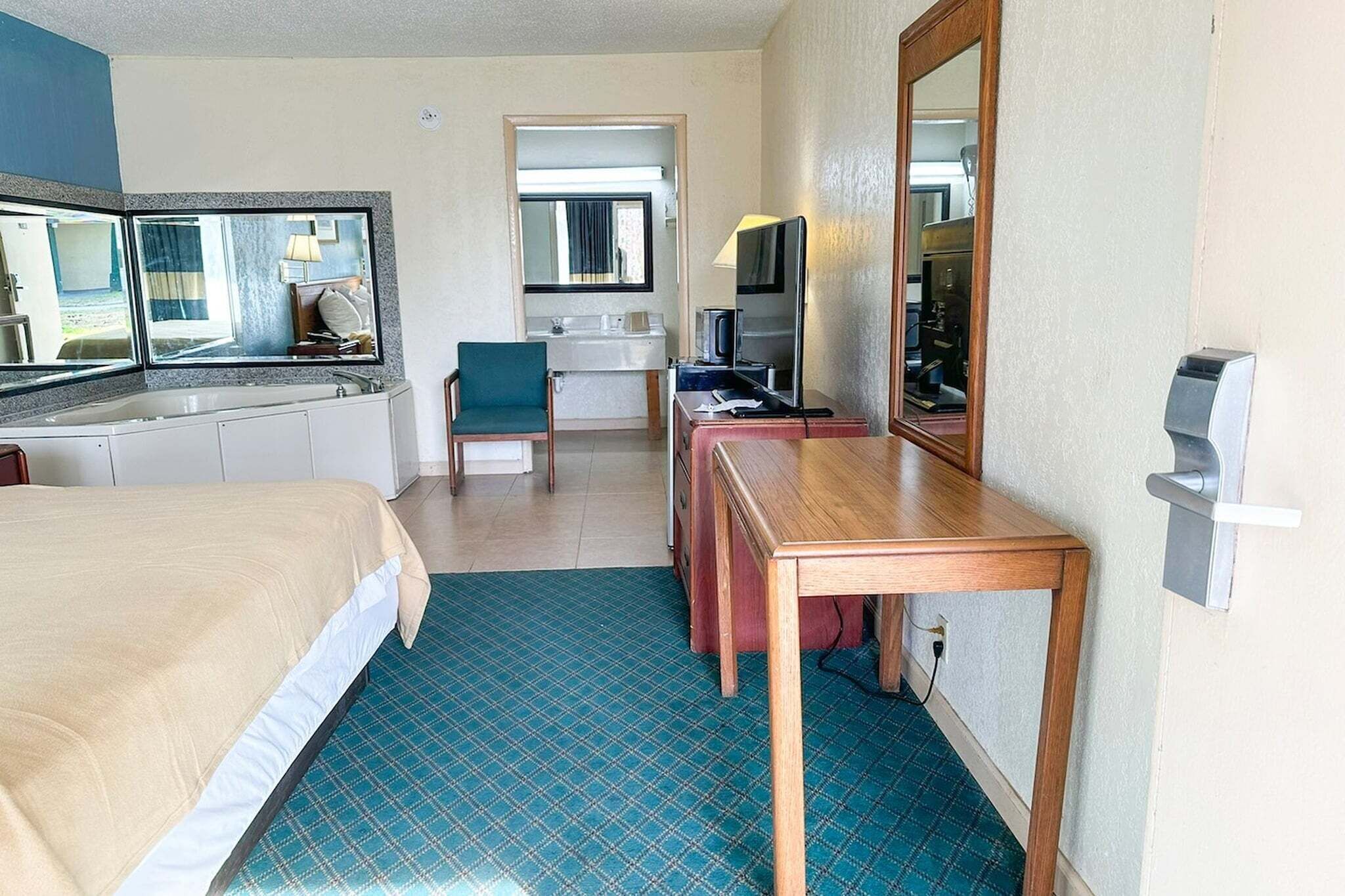A hotel room with a bed, a desk, a chair, a mirror, a sink, and a television.