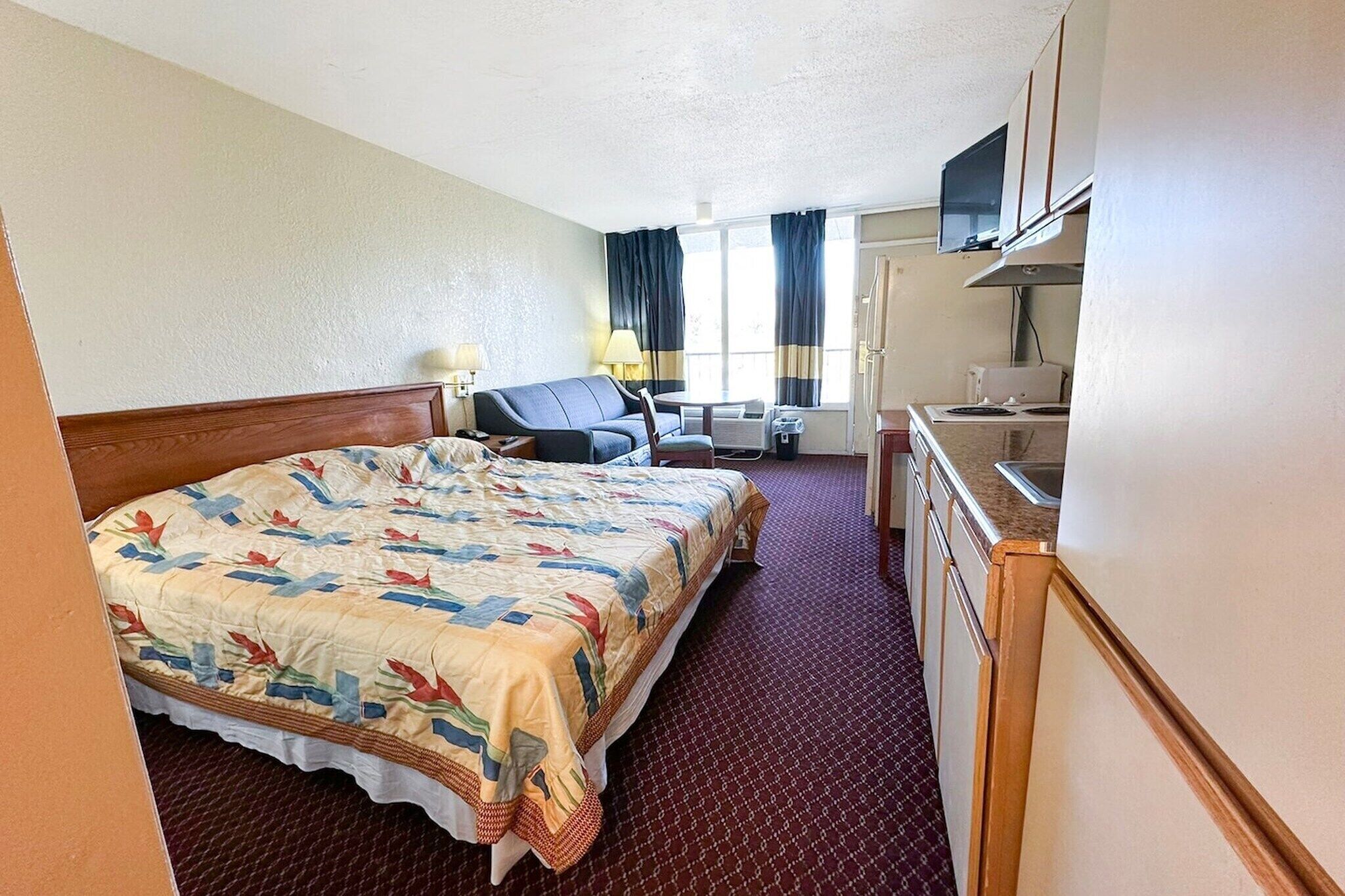 A hotel room with a bed, a desk, a chair, a television, and a kitchenette.
