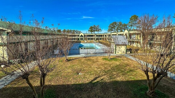 A courtyard with a swimming pool, surrounded by buildings with a green roof and a clear blue sky. - King Bed Smoking with Kitchenette (Milledgeville, GA)