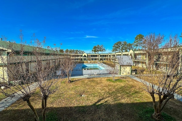 Un patio con piscina, rodeado de edificios con techo verde y un cielo azul despejado.