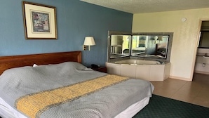 A hotel room with a bed, a bathroom with a sink and mirror, and a framed picture on the wall. - King Bed Smoking with Kitchenette (Milledgeville, GA)