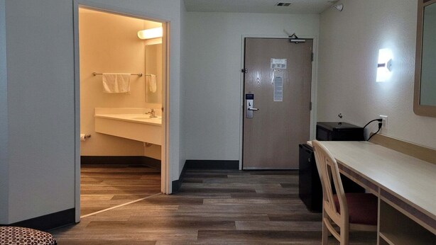 Hotelkamer met houten vloer, een bureau met stoel, een badkamer met handdoekhouder en een deur met slot.
