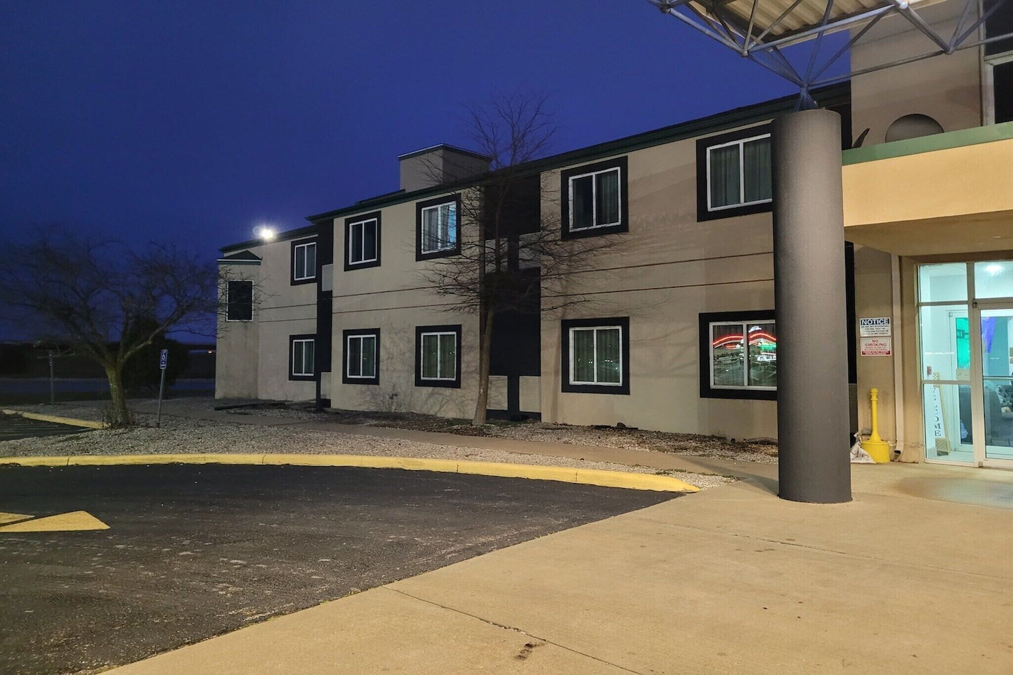 A multi-story building with a parking lot in front, a visible entrance, and a sign indicating a notice area.
