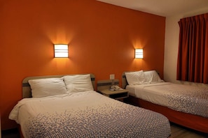 A hotel room with two beds, each with a pillow and a blanket, and two bedside tables with lamps.
