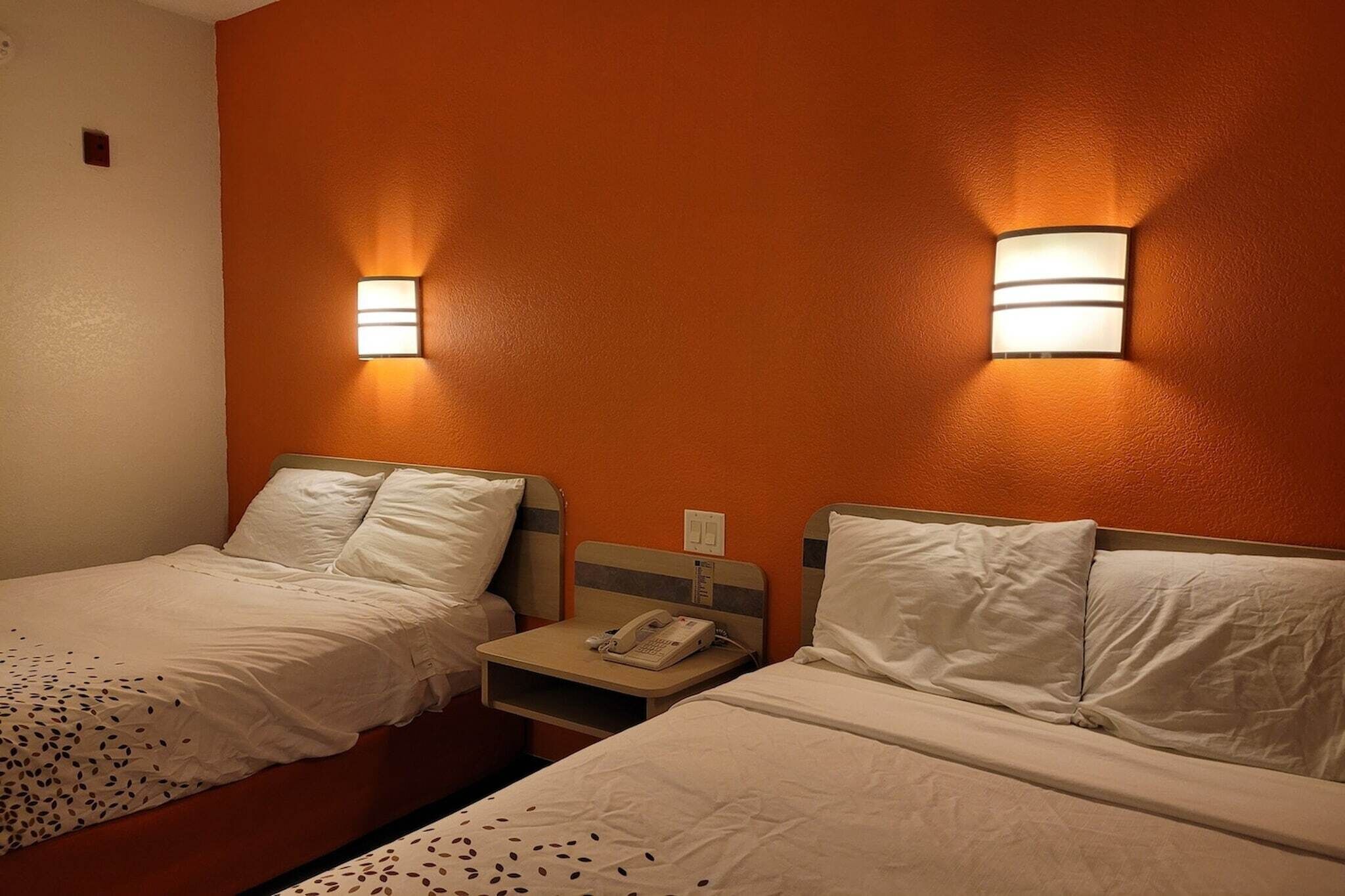 A hotel room with two single beds, each with a nightstand, a phone, and a wall-mounted light fixture.