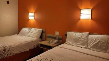 A hotel room with two single beds, each with a nightstand, a phone, and a wall-mounted light fixture.