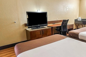 Ein Hotelzimmer mit Fernseher, Schreibtisch, zwei Betten und einem Sessel.
