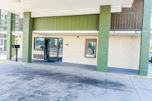 Ein Gebäude mit grüner Fassade, Glastür und erkennbarem Parkplatz.