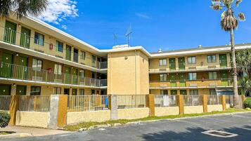 Un motel a più piani con balconi, una torre centrale e palme.