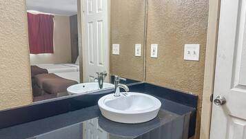 Une salle de bain avec un lavabo blanc, un miroir et une porte donnant sur une chambre.