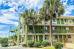 Un hotel de varios pisos con fachada verde, balcones y palmeras.
