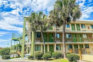 Un hotel de varios pisos con fachada verde, balcones y palmeras.