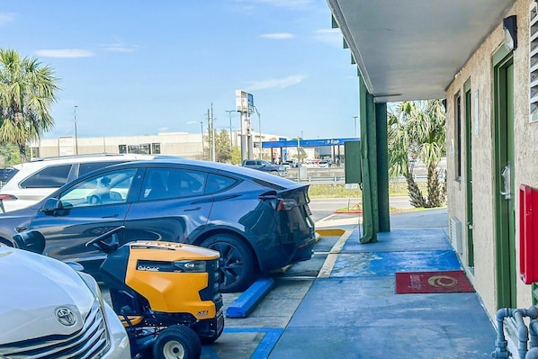 Ein Parkplatz mit Autos und einem gelben Fahrzeug, ein Gebäude mit einer grünen Tür und ein klarer Himmel.
