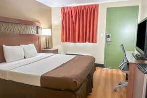 Een hotelkamer met een bed, een bureau met een televisie, een groene deur en een raam met een rood gordijn.