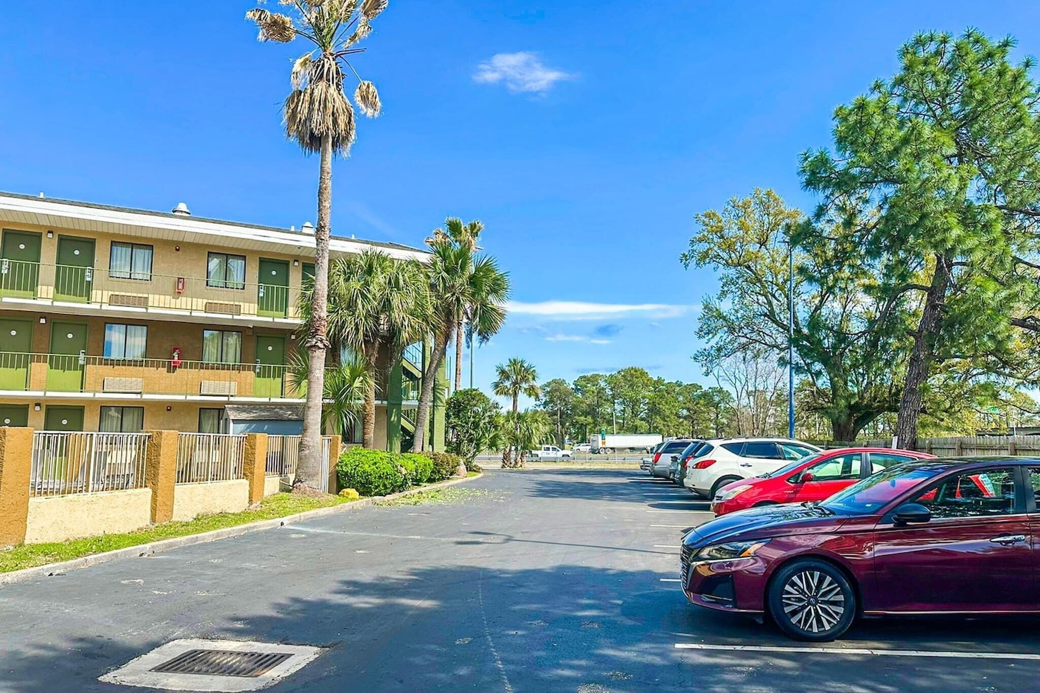 Un hotel de varios pisos con estacionamiento, palmeras y un cielo azul despejado.