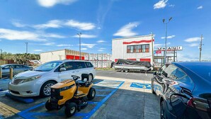 A parking lot with several cars, a golf cart, and a building with a sign that reads 'U+AU!'.