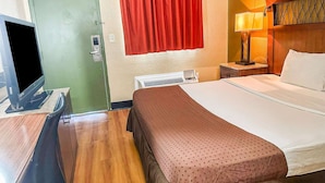 A hotel room with a bed, a television, a heater, and a red curtain.