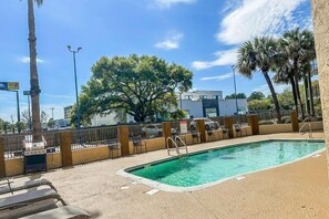 Une piscine entourée d’une clôture, avec des chaises longues et des palmiers.