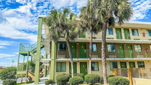 A multi-story hotel with a green facade, balconies, and palm trees.