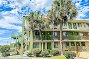 A multi-story hotel with a green facade, balconies, and palm trees.