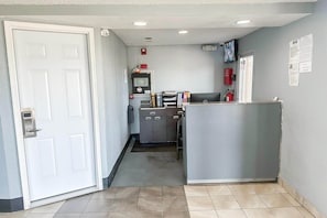 Ein Flur mit einer weißen Tür, einer kleinen Küchenzeile, einem Feuerlöscher und einem an der Wand befestigten Fernseher.