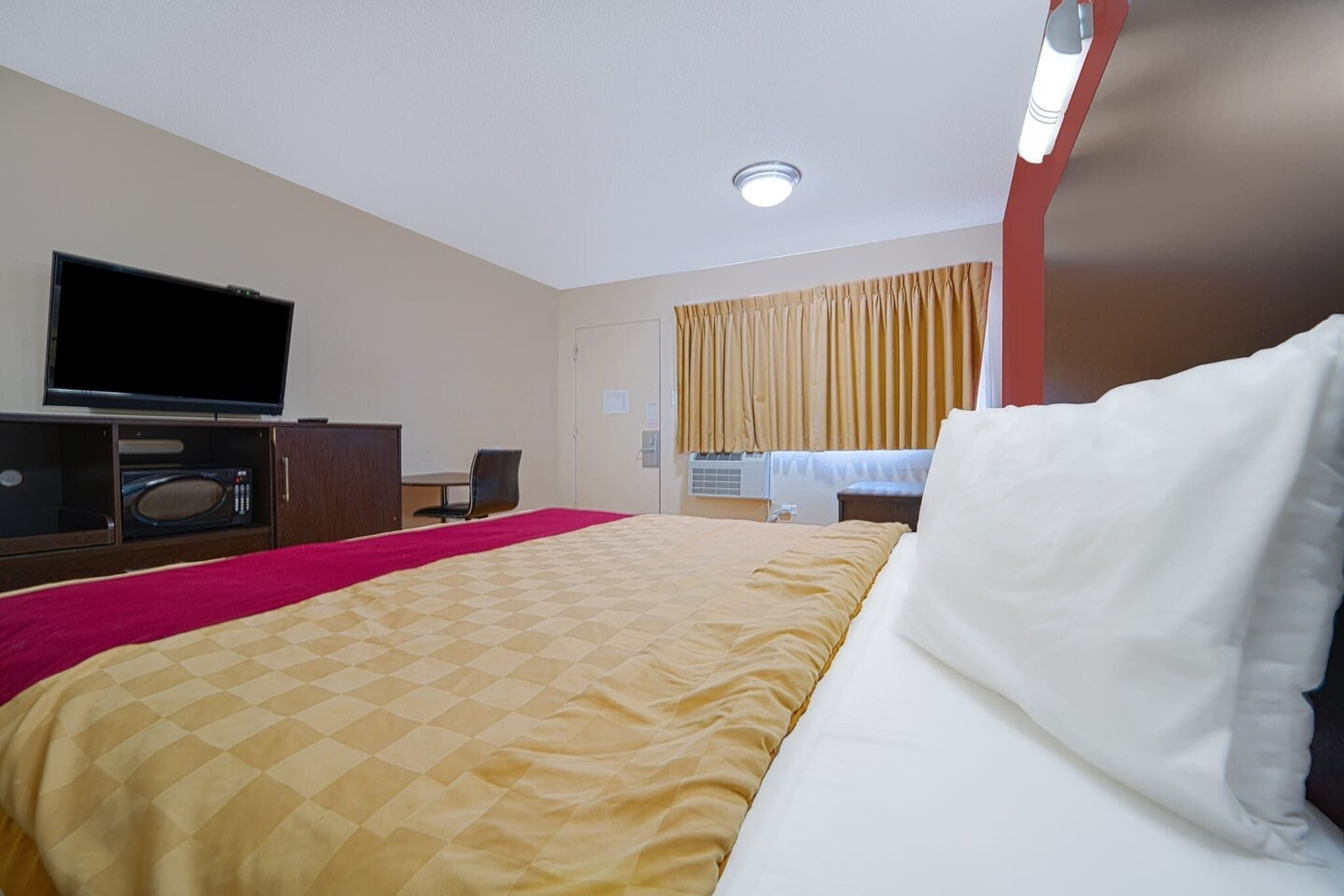 Una habitación de hotel con cama, televisión, escritorio y ventana con cortinas.