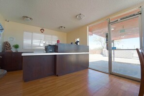 A reception area with a wooden counter, a clock, and a window with blinds. - King Bed|Non-Smoking (Mojave CA)
