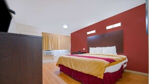 A hotel room with a bed, a desk, a window with curtains, and a ceiling light. - King Bed|Non-Smoking (Mojave CA)