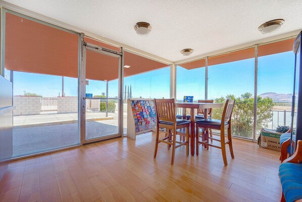 Una habitación amplia con suelo de madera, una mesa de comedor con sillas, ventanas grandes y una puerta corrediza de vidrio que da a un espacio al aire libre.