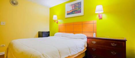 A hotel room with a bed, a nightstand, a dresser, a painting on the wall, and two wall-mounted lamps.
