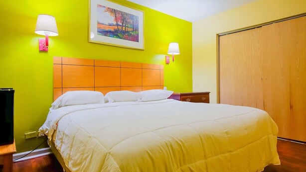A hotel room with a bed, two bedside lamps, a painting on the wall, and a wooden wardrobe.