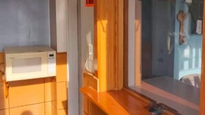A bathroom with a white microwave, wooden vanity, and a glass shower enclosure.