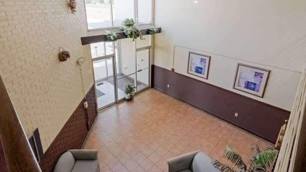 Un hall d’hôtel avec un mur en briques, une entrée avec une porte en verre, un espace salon et des tableaux encadrés accrochés au mur.