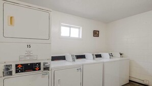 Une buanderie équipée de quatre machines à laver et de quatre sèche-linge superposés, d’une fenêtre et d’un petit tableau accroché au mur.