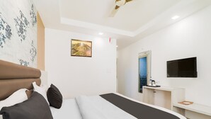 Quarto de hotel com cama, escrivaninha, espelho, televisão e ventoinha no teto.